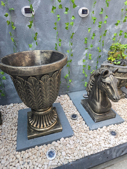 Bronze garden urns on a stone surface with greenery